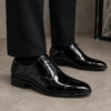 Zapato de novio Oxford en charol negro con brillo espejo sobre caja, ideal para bodas y ceremonias